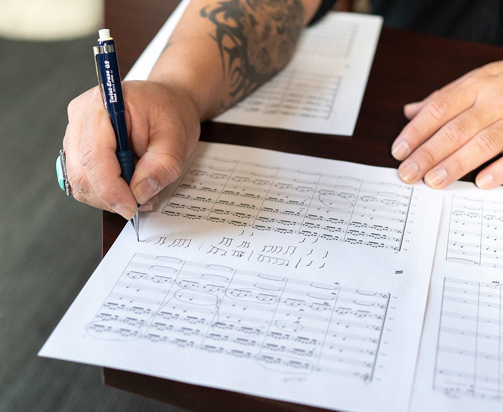 A close up of a hand holding a mechanical pencil over sheet music